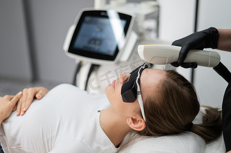 激光手术摄影照片_在光子嫩肤手术中戴护目镜的年轻白人女性。