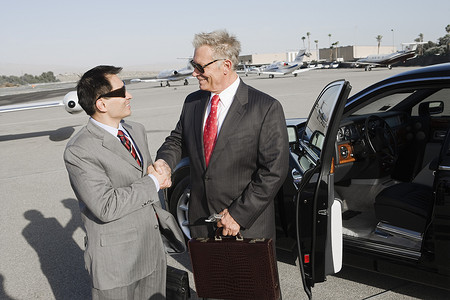 两位成功的商人在机场站在车旁握手