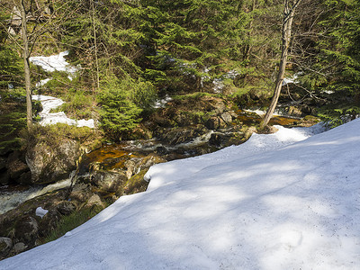 hory摄影照片_捷克共和国 Jizerske hory 的 Cerny Stolpich 溪流，有石头和巨石、草和苔藓、绿色灌木，Jizera 山早春有雪