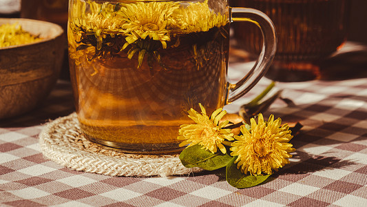 中草药茶摄影照片_桌上玻璃杯中的蒲公英花健康茶。
