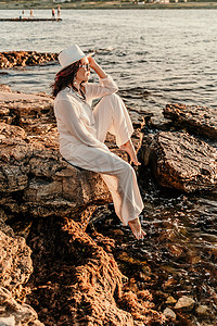 一位穿着白色裤装和帽子的女人站在沙滩上享受大海。