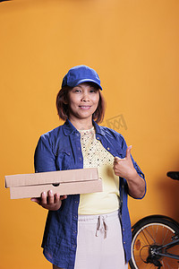 微笑的比萨店送货员在运送带比萨饼的纸箱扁平盒时做批准标志