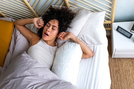 年轻的非洲裔美国妇女早上醒来，在床上打着呵欠伸着胳膊。