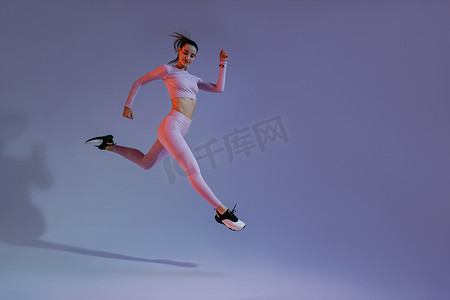 军训进行时摄影照片_在工作室背景下进行有氧运动时，坚定的运动型女性在半空中跑步锻炼