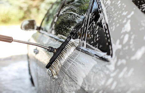 在自助式手动洗车中清洗的银色汽车的一侧。