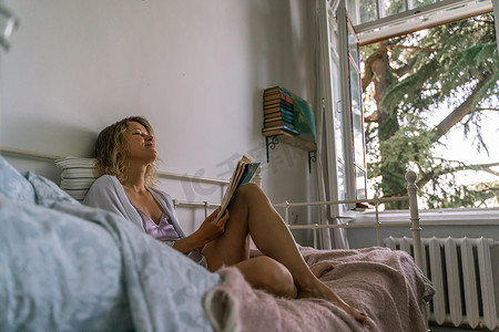 在床上看书的女孩，躺在她的肚子上，在家里的休闲日快乐地微笑着放松