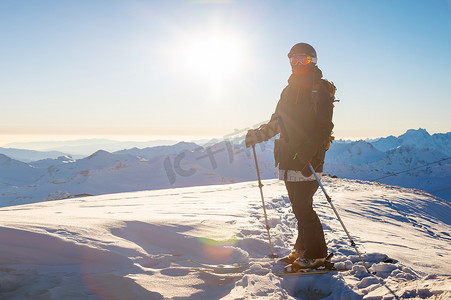 滑雪的成年女孩站在山腰上，欣赏山景，看着镜头，享受阳光明媚的冬日天气。