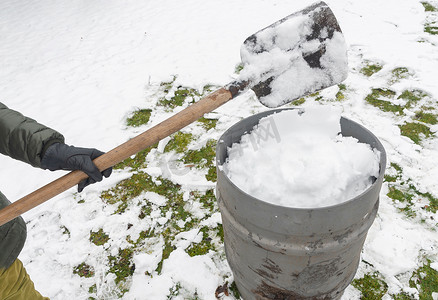 雨桶摄影照片_中年妇女正在用铲子在桶里收集雪，自然资源
