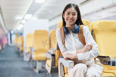 年轻的亚洲美女乘飞机旅行，乘客戴着耳机把手提行李放在飞机座位上方的储物柜里