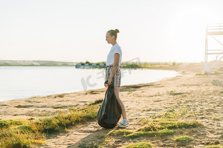 年轻的女志愿者带着袋子和手套捡垃圾、塑料瓶，用大海清理海滩。