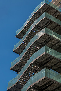 应急出口摄影照片_具有重复结构和反射天空和云彩的现代办公楼中带金属应急梯/防火梯的商务大楼。