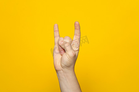 黄色手指手势摄影照片_在黄色工作室背景上做摇滚手势的人的有力手。