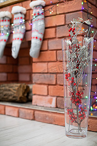 砖砌壁炉背景上带有旋钮的玻璃花瓶，作为圣诞装饰的补充。