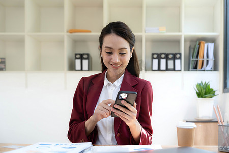 微笑美丽的亚洲女商人分析显示市场变化的图表和图表，并在办公室手持智能手机。