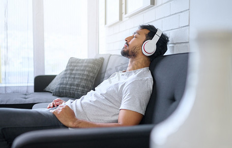 音乐、放松和男人在家里客厅的沙发上戴耳机流媒体广播或播客。