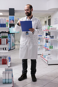 药店工作人员拿着剪贴板检查维生素包装，在纸上写下药物名称