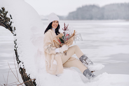 一个穿着米色开衫、开着冬花的女孩正坐在白雪皑皑的公园里的大自然中。