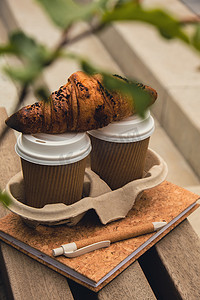 两个带盖的纸杯上放着新鲜出炉的巧克力羊角面包，可以用来盛茶。
