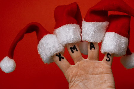 手指穿着圣诞老人红白帽子和红色背景上的文字 XMAS。
