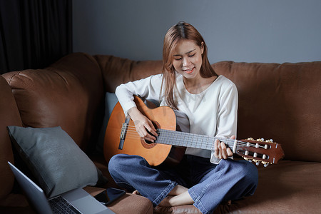 亚洲年轻女性在沙发上弹吉他放松度假压力的画像
