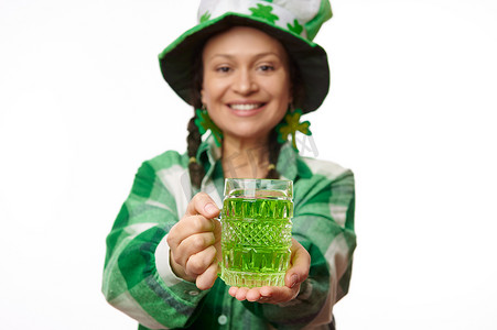 圣帕特里克节的一杯绿色啤酒，在模糊的女人手中，她戴着带三叶草叶子的帽子。