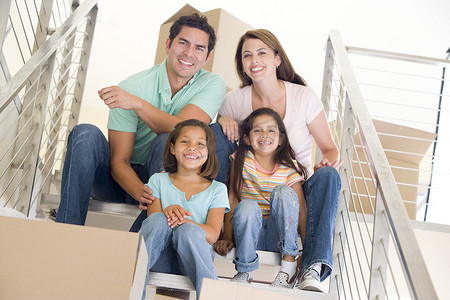 楼梯上搬箱子摄影照片_一家人坐在楼梯上，带着箱子在新家微笑