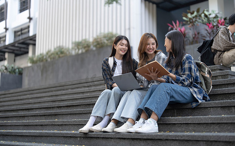 一群亚洲大学生在户外草地上阅读书籍和辅导特殊课程。