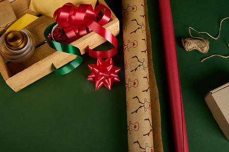 在板条箱旁边特写包装礼品纸，在绿色背景上装饰胶带、丝带和蝴蝶结。