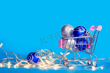 蓝色圣诞平安夜摄影照片_圣诞树球和圣诞花环躺在购物车里