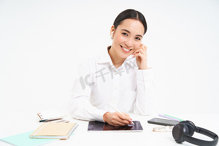 戴着耳机的亚洲女性肖像，在数字平板电脑上工作，签署数字合同，坐在办公室里微笑着，白色背景