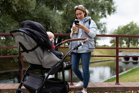 年轻妈妈推着婴儿车在公园散步，手里拿着电话