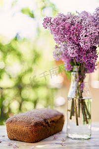 瓶子里的花束摄影照片_阳台上的瓶子里放着一束丁香花，旁边是自制面包