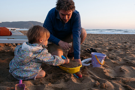 父亲和孩子坐在夕阳下的沙滩上