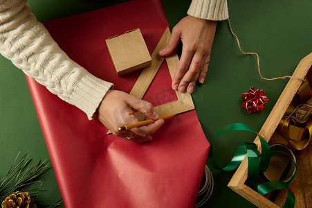 用木铅笔和三角尺的女手在礼品纸上画画，计算包装礼物的数量