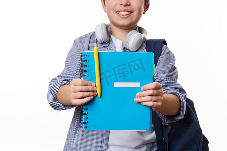 柔和地关注一本蓝色的抄写本，手里拿着黄色的钢笔，一个快乐的少年学生在白色背景中微笑