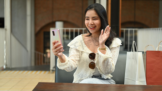 坐在户外咖啡店里，快乐的亚洲女性用手机打视频电话