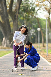 细心的执业护士协助老年女性用三脚拐杖行走。