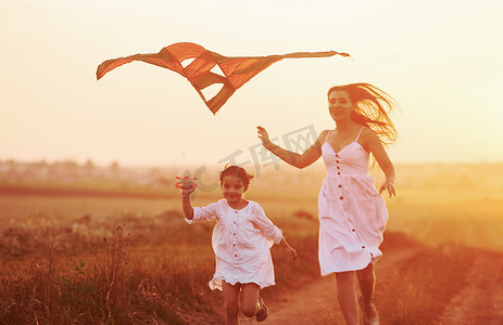 风筝玩具摄影照片_快乐的妈妈和小女儿在户外的田野里玩风筝，玩得很开心