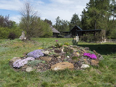 春天的花园里有美丽的岩石花园，盛开着粉红色的福禄考、Armeria maritima、海参、Bergenia 或大象耳朵、康乃馨和其他五颜六色的鲜花和凉亭或凉亭