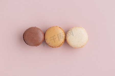 粉红色背景上的三个柔和色的蛋白杏仁饼干，五颜六色的法式饼干图案。 