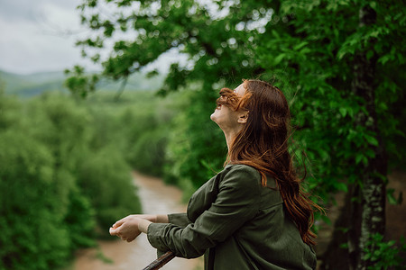 一个红头发随风飘扬的美女站在公园里俯瞰山河