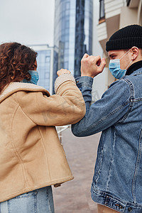 感染摄影照片_一对戴着防护面具的夫妇在检疫时间在商业大楼附近的城市互相问候。