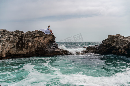 暴风雨中的女人坐在海中的一块石头上。