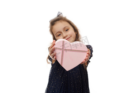 专注于白色背景中一个模糊的正面微笑小女孩手中漂亮的粉红色心形礼盒
