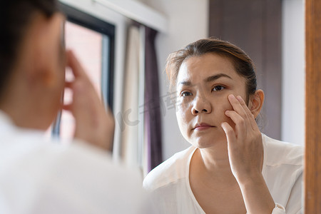 中年亚洲女性看着镜子里的皱纹