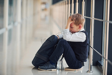 孩子难过摄影照片_穿着制服的男孩独自坐在学校里感到难过。