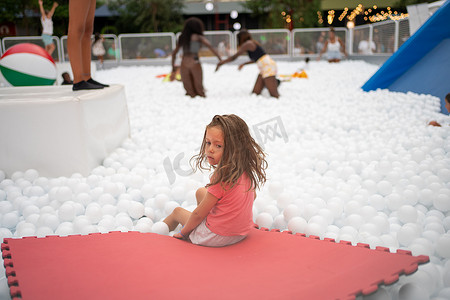 游乐摄影照片_快乐的小女孩在游乐园里玩白色塑料球池。