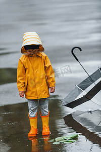 雨后穿着黄色防水斗篷、靴子和雨伞在户外玩耍的孩子