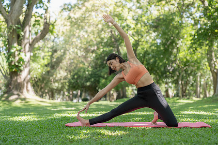 年轻迷人的女孩正在公园中央的健身垫上做高级瑜伽体式。