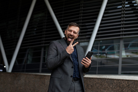在商务中心的背景下，一位成功的微笑的欧洲男记者手里拿着电话走路